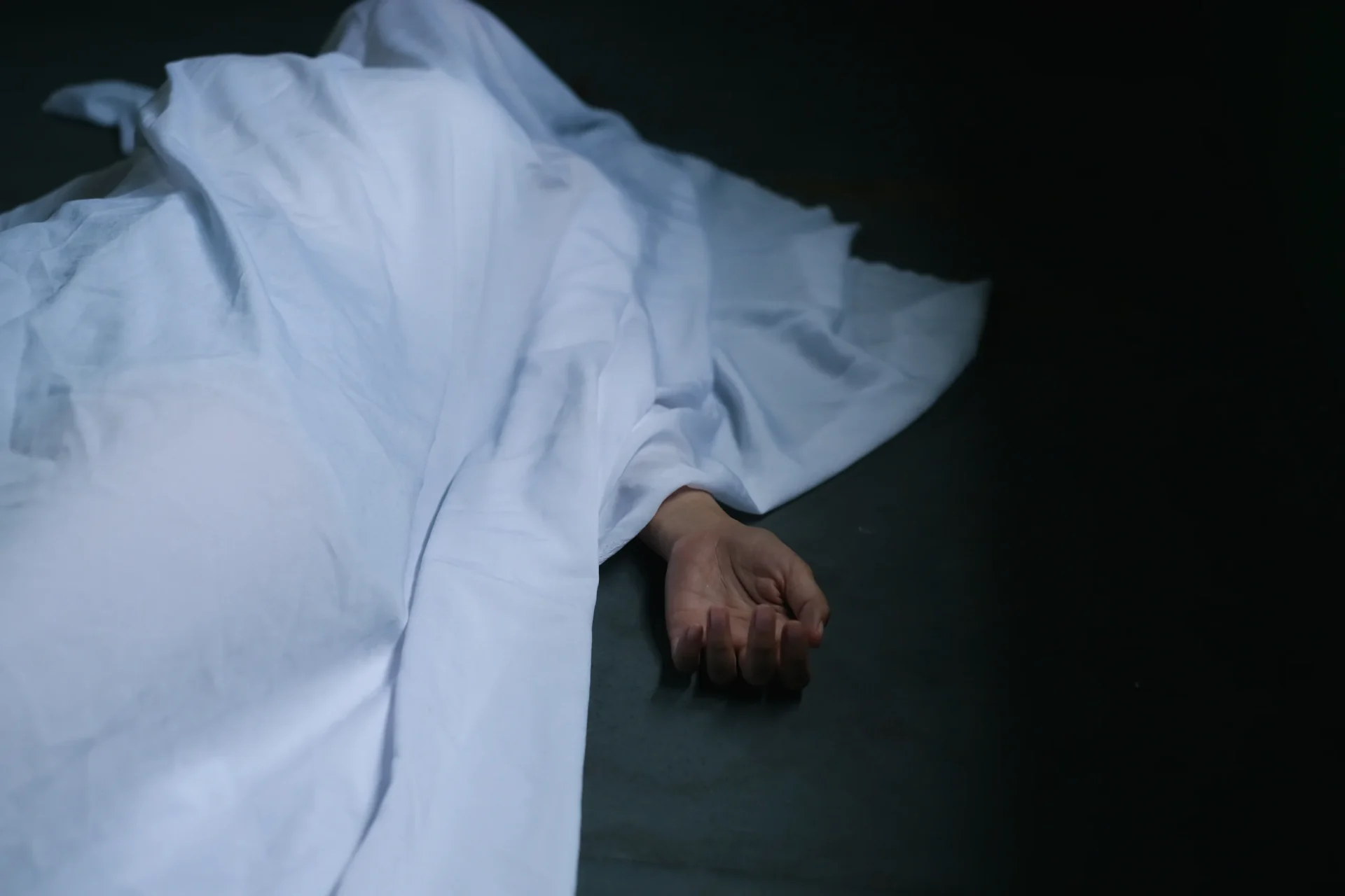 A deceased person's hand shows from under a sheet