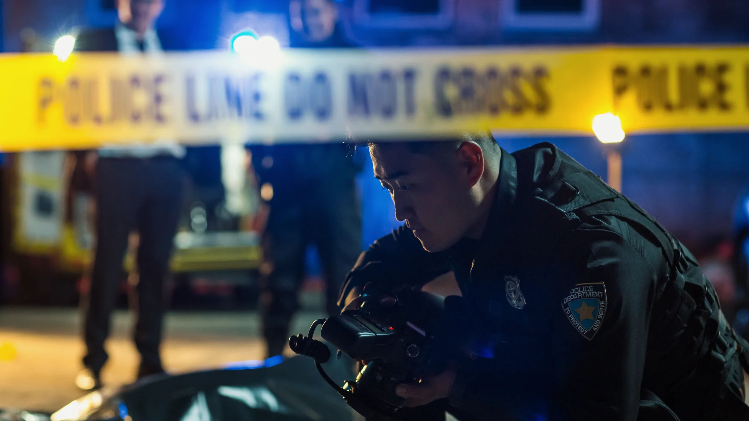A forensic photographer looks at something on the ground behind caution tape