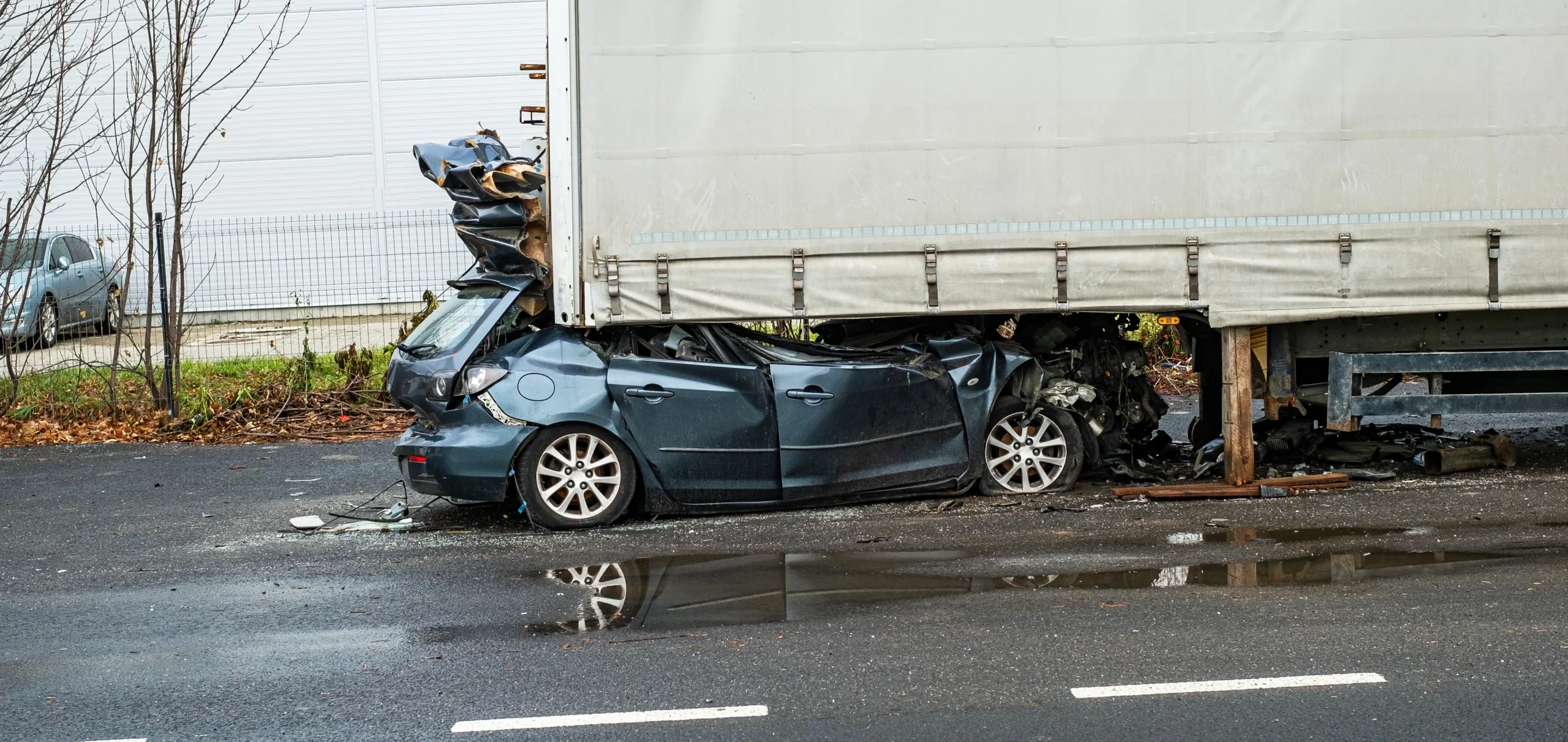 A car is crushed under the back of a semi truck