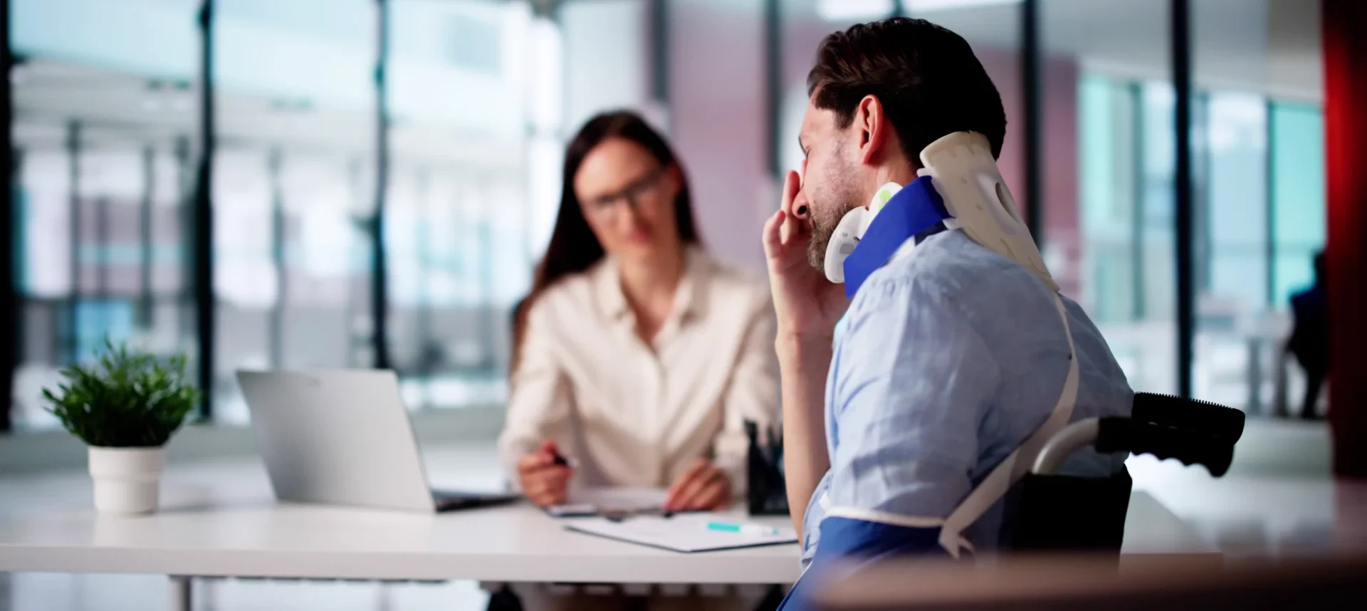 A man in a neck brace sits frustrated at a desk