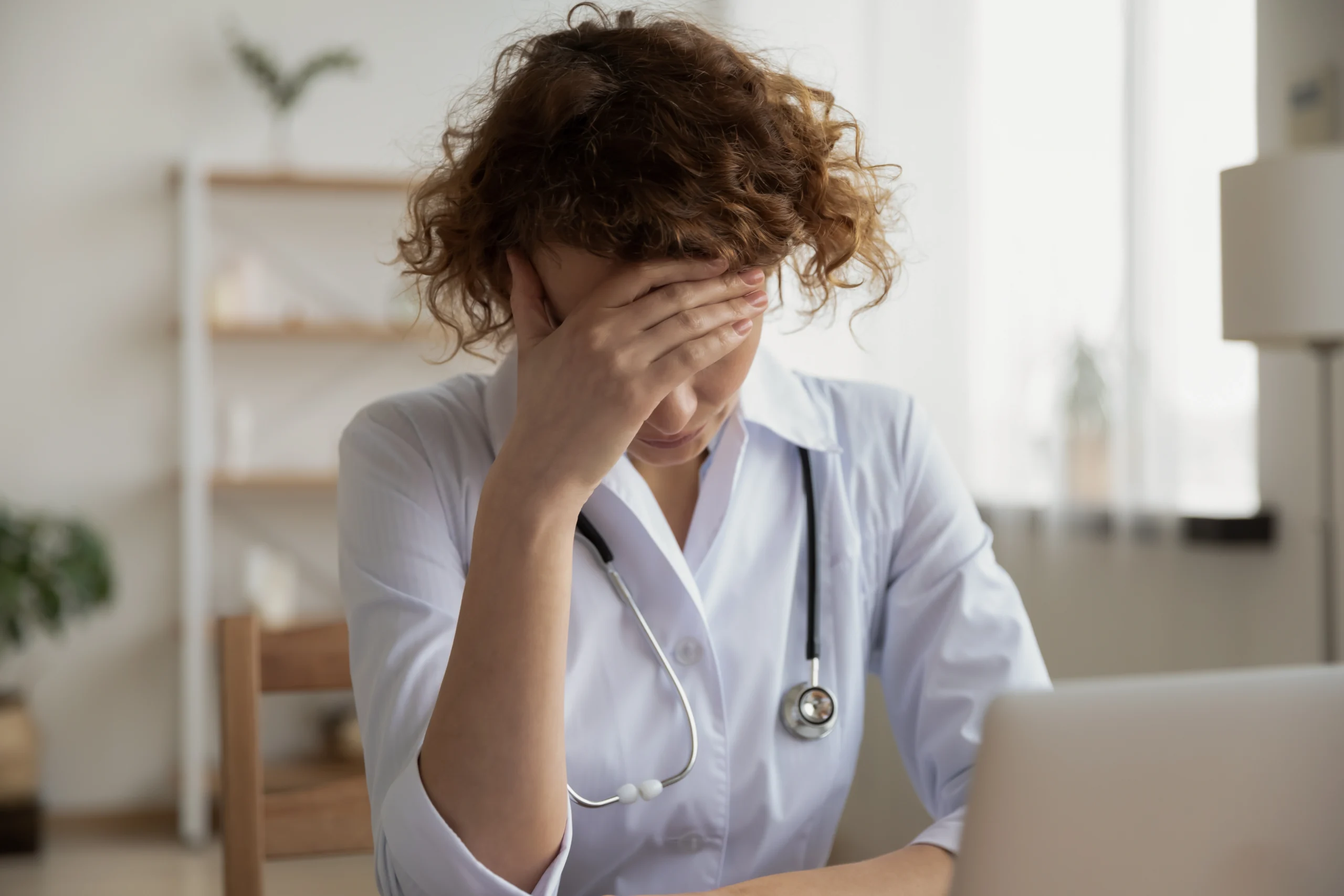 A medical professional holds her head at a desk