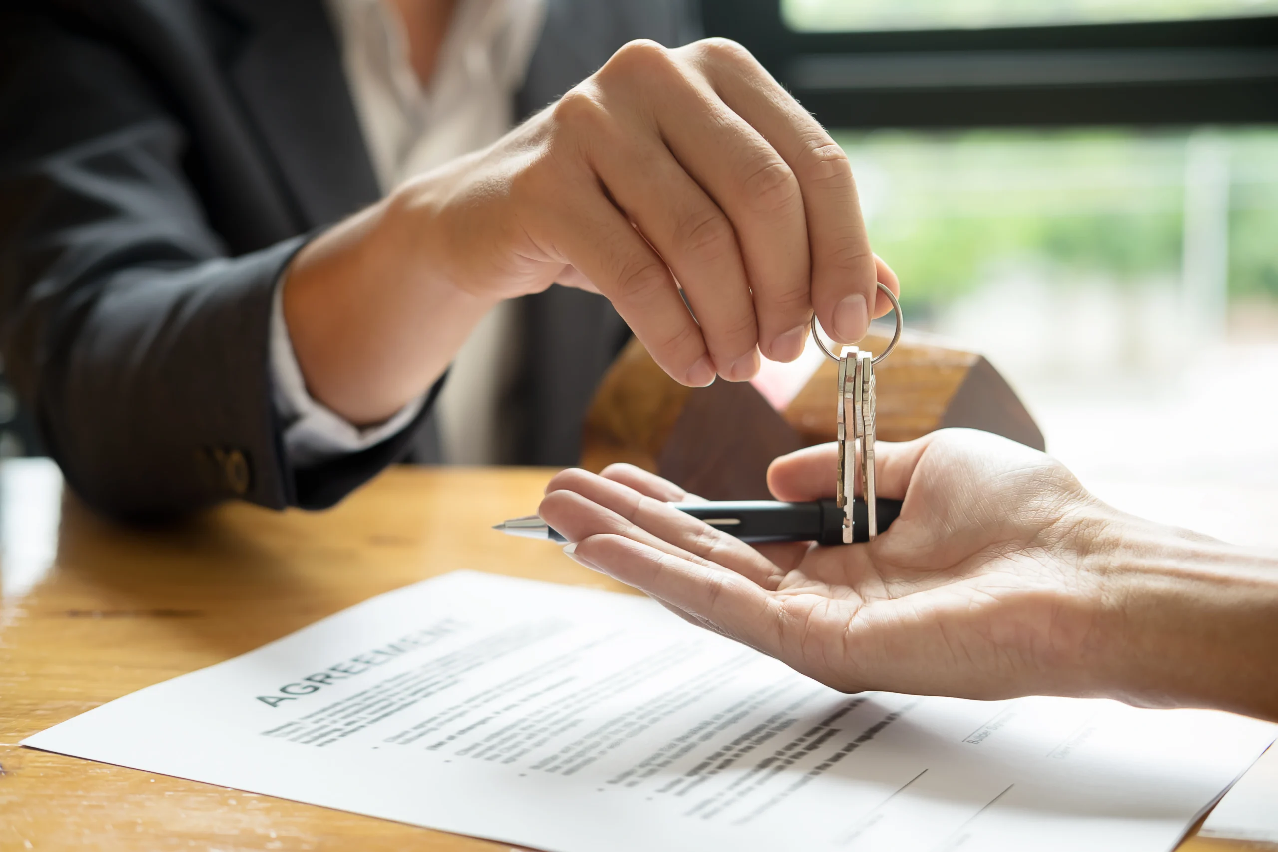 A business person hands another person a set of keys over form labeled Agreement