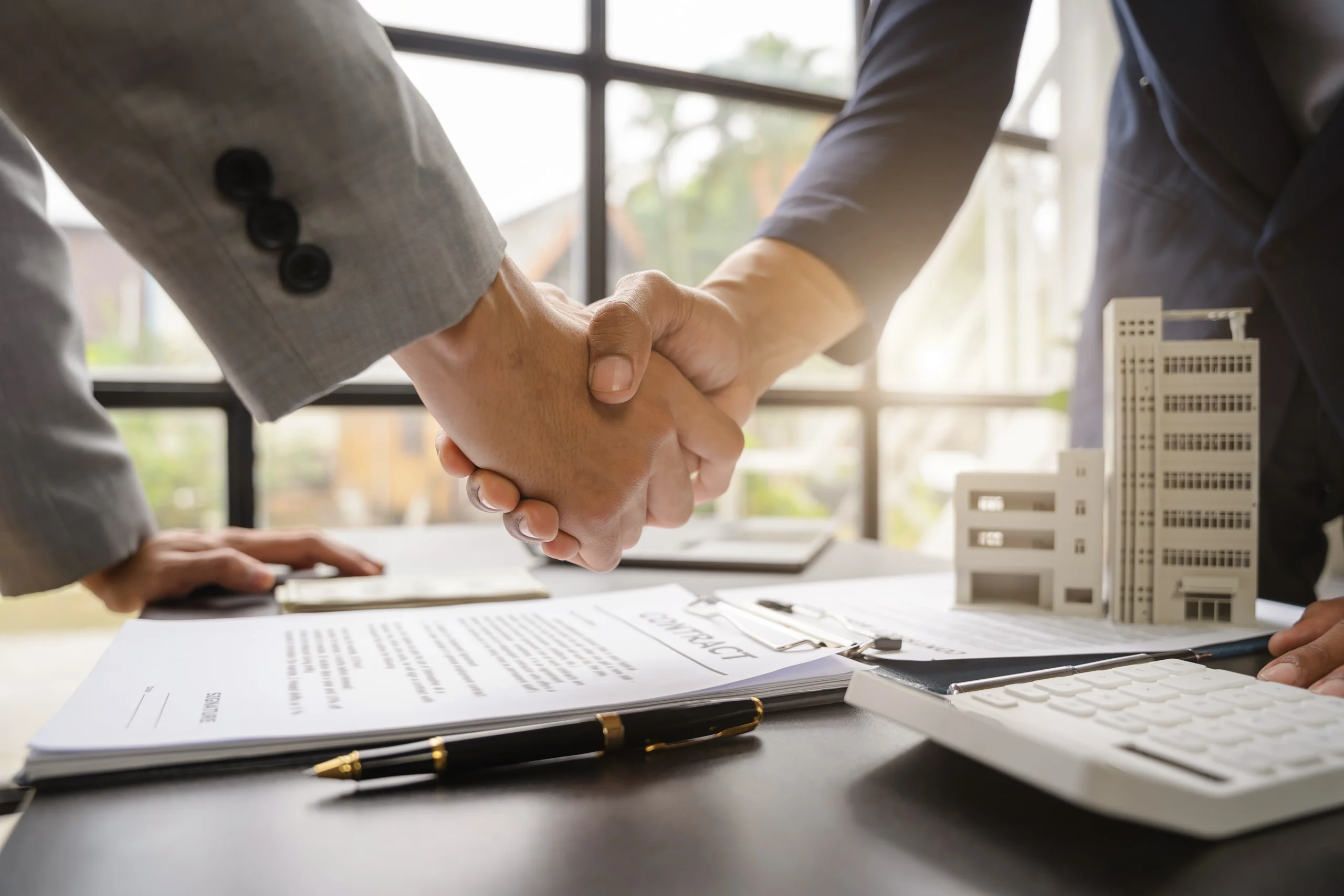 Two business people shake hands over a desk and a contract