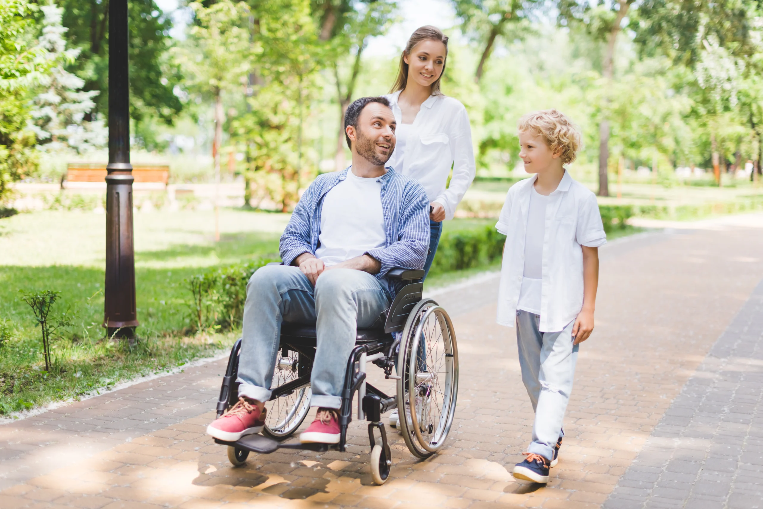 A woman pushes a man in a wheelchair as a child walks alongside them