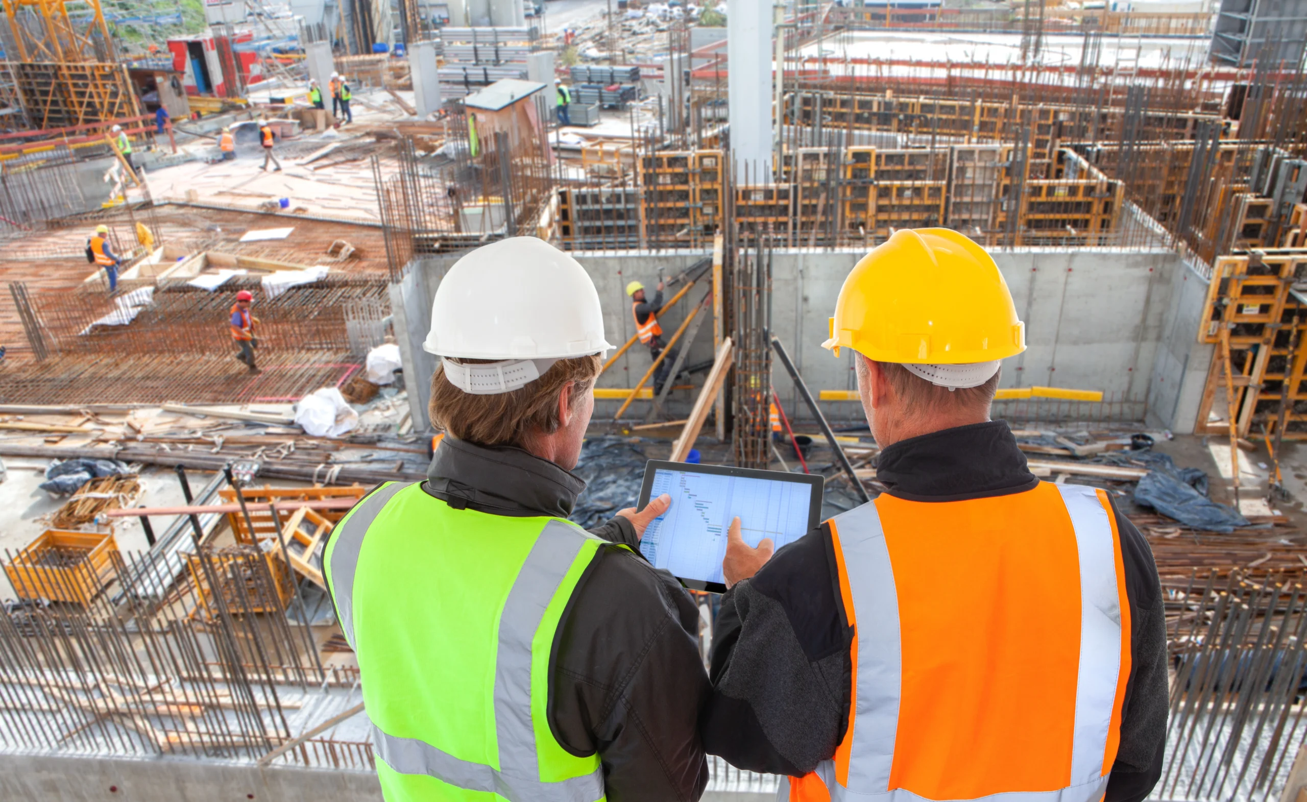 Two construction managers review charts in front of a construction site