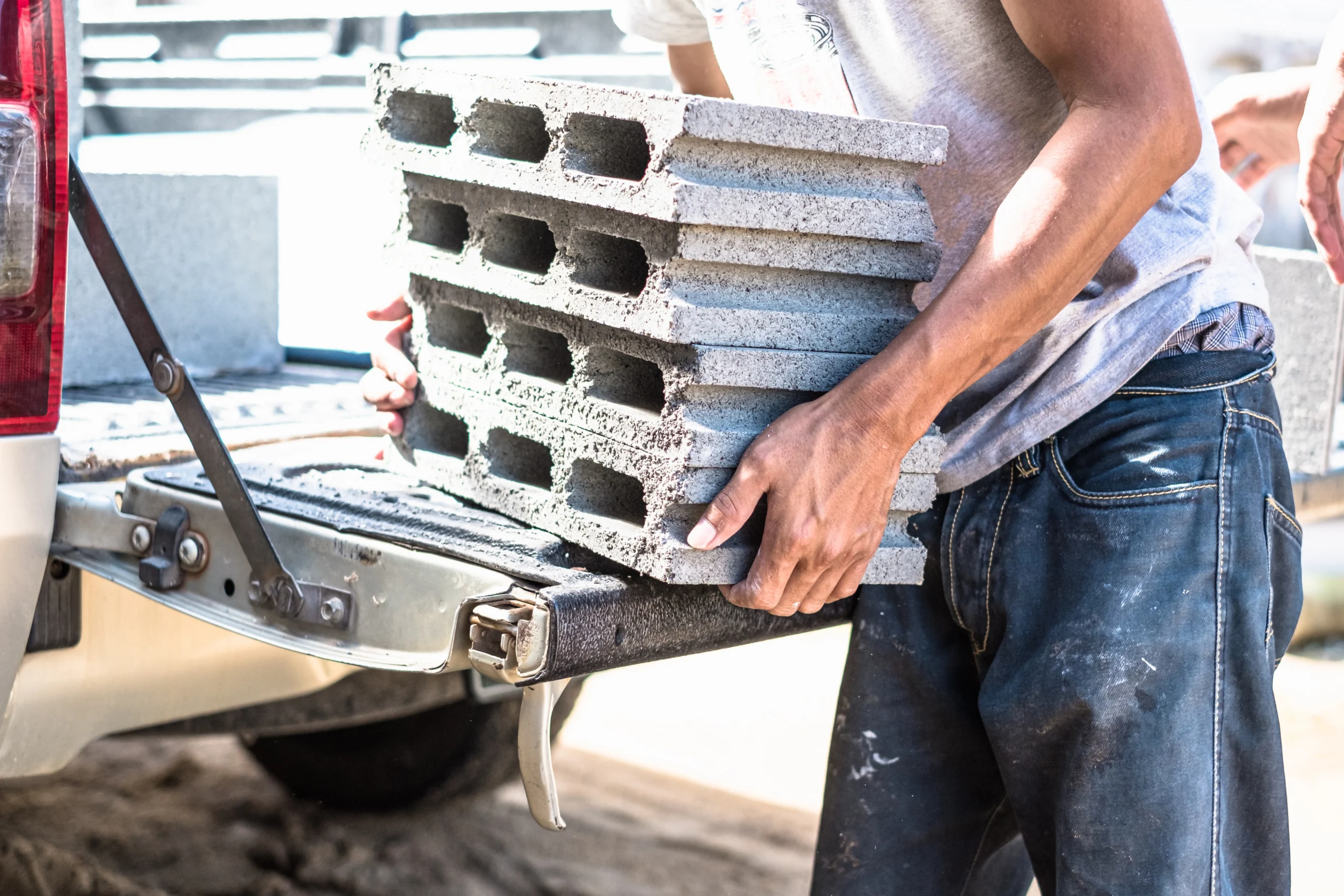 A construction worker loads cement bricks onto the back of a pickup truck